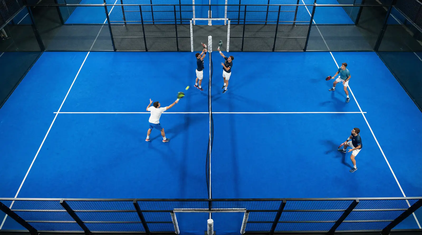 Vista cenital de una pista de pádel profesional con cuatro jugadores en pleno intercambio de bola