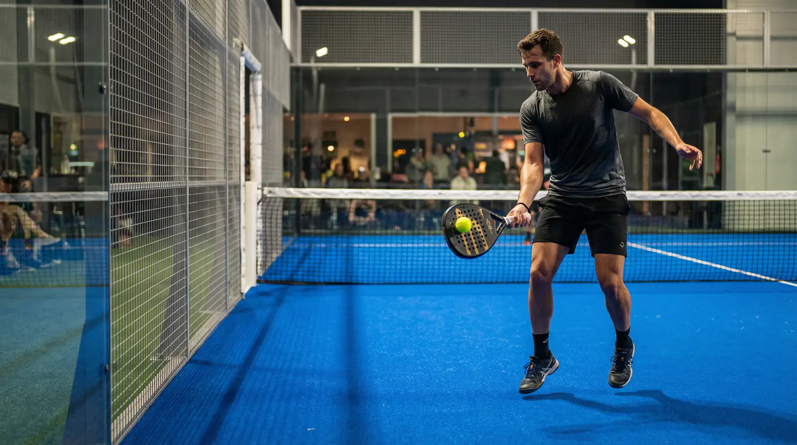 Jugador de pádel profesional ejecutando una volea en pista cubierta con iluminación cenital intensa